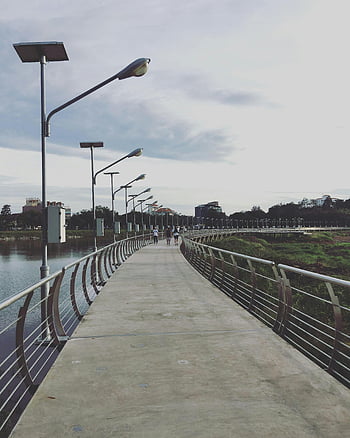 urban bridge, Khon Kaen, Thailand, riverside view, scenic walkway, people walking, middle of pathway, serene view, street lamps, concrete path, waterfront promenade