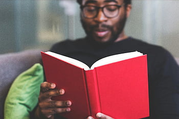Mann liest ein Buch, Rotes Buch, fokussierter junger Mann, Innenlesen, Lernen und Entspannung, Mann auf Sofa, drinnen lesen, junger Mann liest, Buch lesen, Entspannung in Innenräumen, konzentriertes Lesen