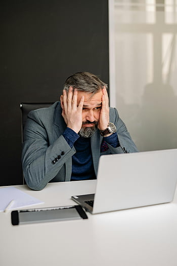 stressed man, office desk, hands on face, laptop screen, adult man, suit, work stress, professional setting, office environment, computer work, workplace stress