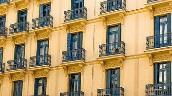 yellow residential building, elegant yellow building, intricate balcony design, blue shutters, residential facade, yellow building exterior, architectural details, urban architecture, classic design, European style, residential architecture