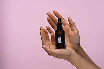skincare, serum bottle, brown glass bottle, dropper bottle, hands holding, pink backdrop, close-up, skincare product, beauty, cosmetic, serum