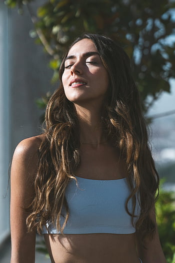 woman in white crop top, smiling eyes closed, serene woman, long hair, sunlight, meditating in nature, mindfulness, tranquility, outdoor portrait, natural light, peaceful moment