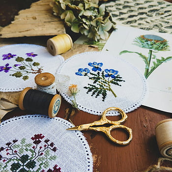 kruissteekborduurwerk, bloemen borduurwerk, spoelen van draad, schaar, rustieke tafel, handgemaakte kunst, levendig borduurwerk, borduurhoepels, borduurgaren, Borduurgereedschap, borduurmotieven