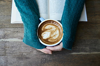 hrnek na kávu, latte art, Ruce drží hrnek, otevřená kniha, dřevěný stůl, keramický hrnek, latte, Složité latte umění, Útulná scéna, Čtení kávy, Svetr rukávy