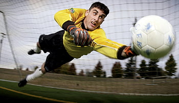 kiper sepakbola, menangkap bola, lapangan sepak bola, aksi olahraga, sarung tangan kiper, jersey kuning, jaring sepak bola, olahraga di luar ruangan, pria atletis, pertandingan bola, fotografi olahraga