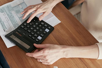 woman, calculator, reviewing bills, home office, financial stress, money management, personal finance, paperwork, desk, indoor, close-up