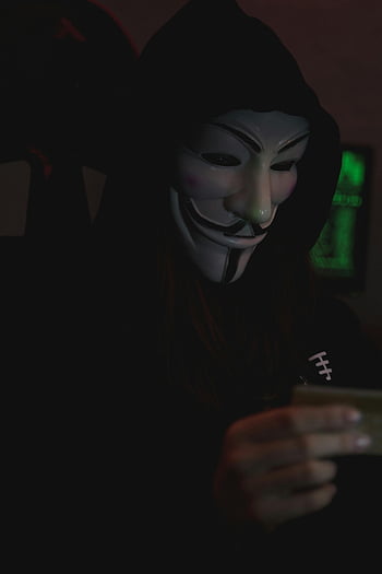 Guy Fawkes mask, digital anonymity, close-up view, laptop, secrecy, anonymous individual, hooded person, dark setting, cyber security, online privacy, hacker