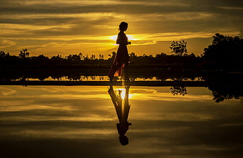 sunset silhouette, woman silhouette, calm water, sunrise reflection, serene scene, lake reflection, golden hour, peaceful moment, natural beauty, outdoor photography, tranquil setting