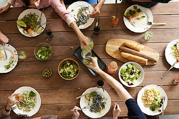 dining table, pasta dishes, salads, group meal, overhead shot, woman pouring juice, glass, wooden table, shared food, meal gathering, dining experience