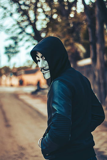 man wearing hoodie, Guy Fawkes mask, urban street, mystery, intrigue, hooded figure, mask wearer, street scene, mysterious person, urban atmosphere, hooded individual