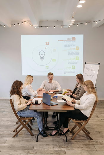 liiketoimintaryhmä, yhteistyö, esittely, hyvin valaistu toimisto, ryhmäkokous, ihmiset istuvat, tuolit, pöytä, toimistoympäristö, ryhmäkeskustelu, projektivaiheet