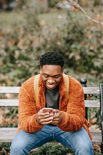 mladý černoch, usmívající se, chytrý telefon, městský park, Veselý muž, lavice, venku, Lush Park, Neformální outfit, využití technologie, městského životního stylu