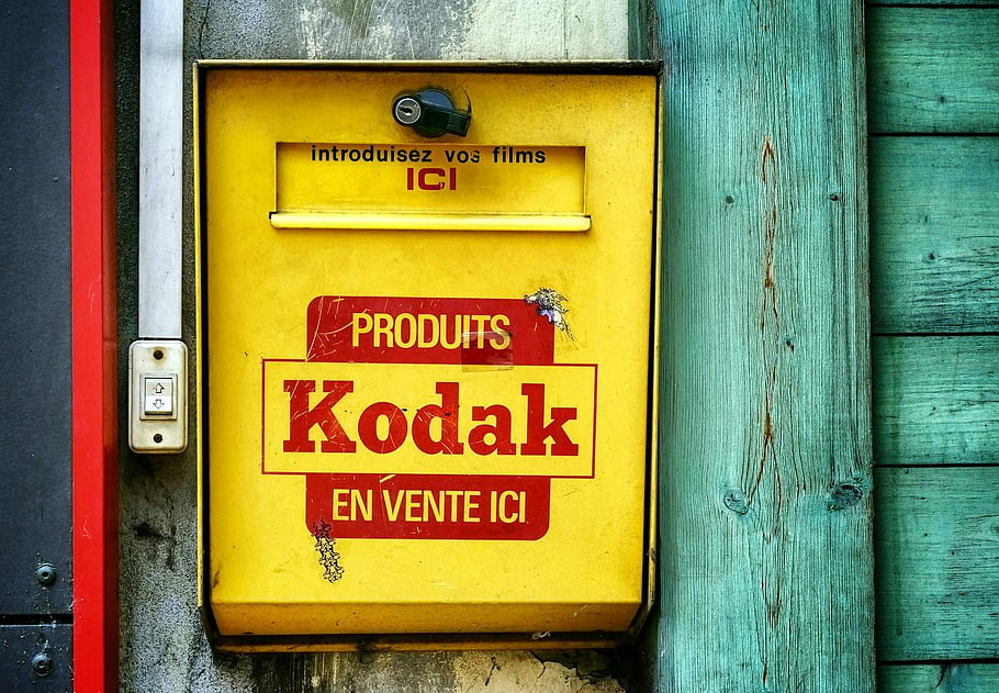 ročník Kodaku, schránka na film, žlutá barva, Rustikální dřevěná zeď, Produkty Kodaku, prodám zde, detailní fotografie, retro fotoaparát, filmové fotografie, žlutá a červená, Vintage reklama
