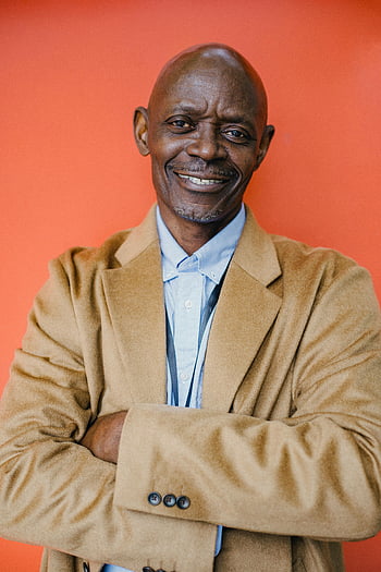 munter moden mand, velklædt sort forretningsmand, foldede arme, selvsikkert smil, studio portræt, Stilfuld mand, Professionel påklædning, orange baggrund, selvsikker positur, Ældre professionel, studiofotografering