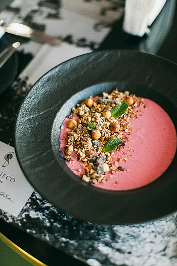 granola yogurt bowl, vibrant pink smoothie, black plate, healthy breakfast, round black saucer, granola topping, mint leaves, yogurt bowl, pink smoothie, black dish, healthy meal