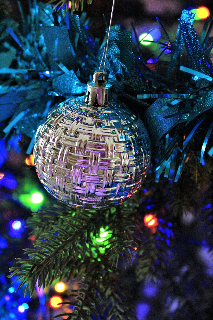 silver bauble, green Christmas tree, close-up ornament, colorful lights, holiday spirit, festive decoration, Christmas decoration, silver ornament, tree lights, holiday season, Christmas tree ornament