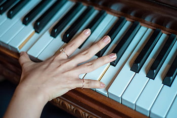 brown wooden piano, two fingers playing, hand with rings, piano keys, musical elegance, craftsmanship, close-up piano, piano music, elegant hand, piano playing, musical instrument