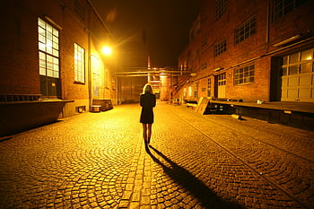 woman walking, night street, illuminated alley, dramatic shadows, city alley, back view, cobblestone street, urban night, lone woman, brick buildings, street light