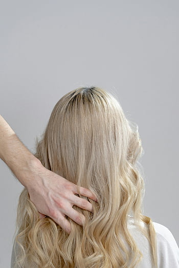 blonde hair, hand touching hair, woman with blonde curls, hair salon setting, styled hair, gentle styling, blonde curls, hair care, hair styling, woman's hand, hair salon