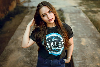 kvinde iført t-shirt, ung kvinde, Langt brunettehår, afslappet tøj, udendørs, selvsikker positur, Oakley T-shirt, afslappet mode, udendørs mode, kvindelig model, gadestil