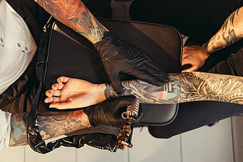tattoo artist, detailed ink design, client's arm, tattoo parlor, overhead view, tattooing process, black gloves, arm tattoo, tattoo machine, detailed tattoo, tattoo studio