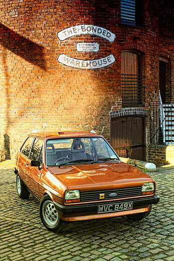 Ford 5-door Hatchback, classic orange car, historic brick warehouse, cobblestone pavement, vintage vehicle, Ford logo, AA badge, WVC 849X, The Bonded Warehouse, Stourbridge Navigation Trust, classic car photography