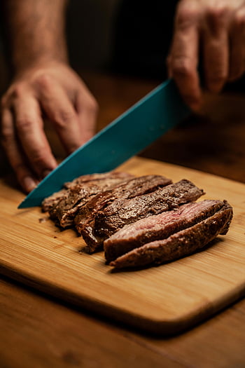 Šéfkuchař krájení steak, dřevěné prkénko, Kulinářská přesnost, Dokonale vařené steak, řezání masa, Modrý nůž, hnědá deska, Příprava steaku, ruce šéfkuchaře, fotografování potravin, Klik steaku