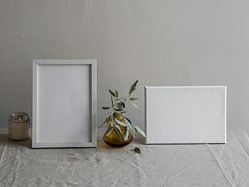 blank photo frame, table, vase, candle, minimalist setting, elegant still life, minimalist decor, white tablecloth, decorative objects, simple composition, indoor scene