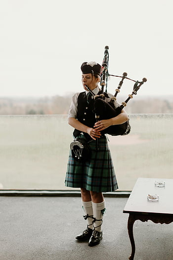 Scottish piper, bagpipes, traditional Scottish attire, woman playing bagpipes, indoor setting, tartan kilt, Scottish music, cultural performance, traditional instrument, Scottish tradition, indoor event