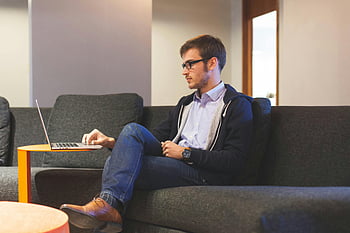 Mann, Sitzung, Schwarze Couch, Freizeitkleidung, Arbeiten aus der Ferne, Laptop, Couch, drinnen, junger Mann, Heimarbeit, Gelegenheitsarbeit
