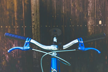 blue bicycle handlebar, black handlebar, blue brake levers, wooden backdrop, detailed view, bicycle handlebar, blue and black, bike handlebar, bicycle accessories, outdoor cycling, bike parts