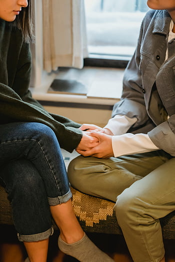 Kvinder, der holder hænder, trøstende gestus, indendørs indstilling, kvindeligt venskab, følelsesmæssig støtte, Hjemmemiljø, uigenkendelig kvinde, forstyrret ven, Sidder sammen, afslappet tøj, Komfort og omhu