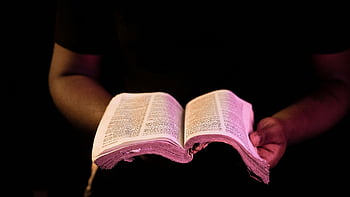 person holding Bible, open Bible, dark background, close-up, religious text, spiritual reading, hands holding book, sacred scripture, faith symbol, religious imagery, spiritual practice