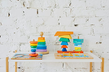 colorful stacking toys, wooden toys, vibrant toys, minimalist table, white table, white brick wall, educational toys, children's toys, stacking blocks, toy display, indoor playroom
