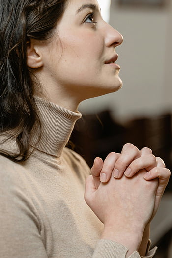 woman praying, close-up view, clasped hands, serene expression, turtleneck, prayer, faith, spirituality, peaceful, contemplation, religious