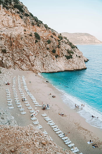 Pláž Antalya, lehátka, tyrkysové vody, Skalnaté útesy, plážová lehátka, horský výhled, Antalya Turecko, Relaxace na pláži, přímořská krajina, Plážová hora, Lounge židle pláž