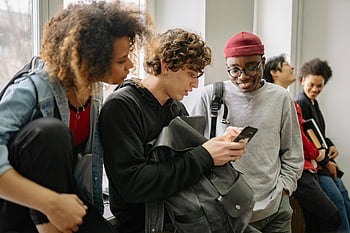 大学生、 多様なグループ、 屋内設定、 スマートフォン、 ぶらぶら、 若年成人、 カジュアルな服装、 グループの相互作用、 テクノロジーの使用、 懇親会、 教育