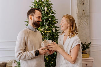 joululahja, hymyilevä pari, koristeltu joulukuusi, lomakausi, Mies antaa lahjan, Nainen saa lahjaa, juhlava ilmapiiri, lämmin hetki, riemu, sisäjuhla, lomahenki