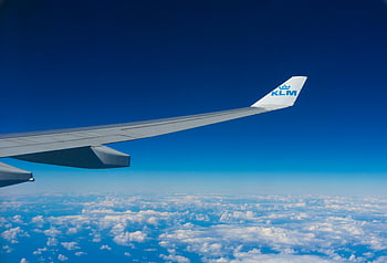 KLM plane, airplane wing, flying above clouds, clear blue sky, KLM logo, white and blue plane, high altitude, aircraft in flight, sky view, cloudscape, aviation photography