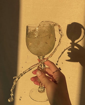 wine glass, splashing drink, warm sunlight, crystal glass, liquid splash, hand holding glass, shadow, sunlight reflection, drink spill, elegant glassware, refreshing moment