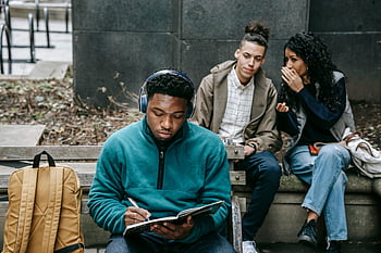 multiracial students, gossiping, black man, notepad, park bench, friends chatting, casual academic vibe, studying, outdoor setting, social interaction, diverse group