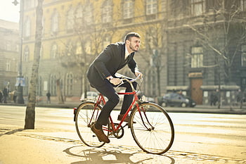 man in black suit, riding bicycle, city street, urban commute, businessman in suit, red bicycle, bright city street, professional cyclist, city life, modern commuter, street scene