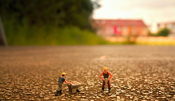 miniature toy construction workers, selective focus photography, two men builder figurines, close-up miniature toys, textured surface outdoors, daylight photography, construction worker figurines, outdoor miniature scene, toy construction workers, miniature construction scene, outdoor toy photography