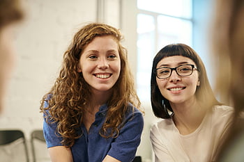 woman wearing blue polo shirt, smiling young women, friendship, happiness, indoors, two women, casual setting, positive emotions, group interaction, social connection, friendly atmosphere
