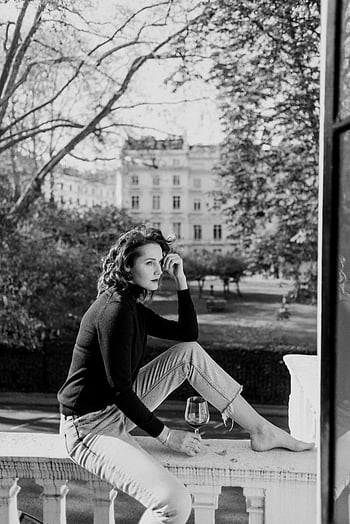 woman with wine, terrace, balcony, leisure time, tranquility, glass of wine, outdoor relaxation, black and white photo, urban setting, sitting, contemplative mood