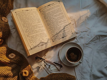 เปิดหนังสือ, กาแฟหนึ่งแก้ว, เสื้อโค้ตถัก, การตั้งค่าที่สะดวกสบาย, หนังสือคลาสสิก, กาแฟอุ่น ๆ, แว่นตา, เวลาอ่านหนังสือ, ช่วงเวลาแห่งการผ่อนคลาย, แสงไฟอ่อน ๆ