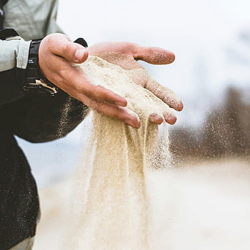 Mann schüttet Sand, Hände sieben Sand, symbolisiert Zeit, Natur, wüstenähnliche Umgebung, Sandkörner, Mantel, Outdoor-Szene, natürliche Elemente, Zeitpassage, Sandfluss