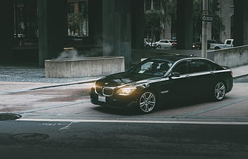 Black BMW sedan, concrete curb, city streets, twilight, luxury car, modern city life, urban design, street scene, car headlights, urban environment, cityscape