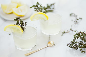 Pití citronového tymiánu, skleněné šálky, letní občerstvení, bílé pozadí, detail, osvěžující nápoj, plátek citronu, tymiánový ozdoba, mramorový povrch, zlatá lžíce, ledové kostky