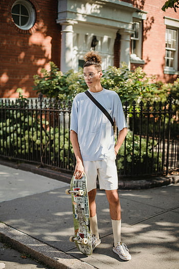 adolescente etnico alla moda, skateboard, giorno soleggiato, marciapiede della città, giorno d'estate, Posa rilassata, contesto urbano, Abbigliamento casual, bicchieri, acconciatura, stile di strada